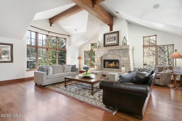 living area featuring beamed ceiling, wood finished floors, a healthy amount of sunlight, and a glass covered fireplace