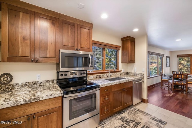 kitchen featuring baseboards, recessed lighting, brown cabinets, stainless steel appliances, and a sink