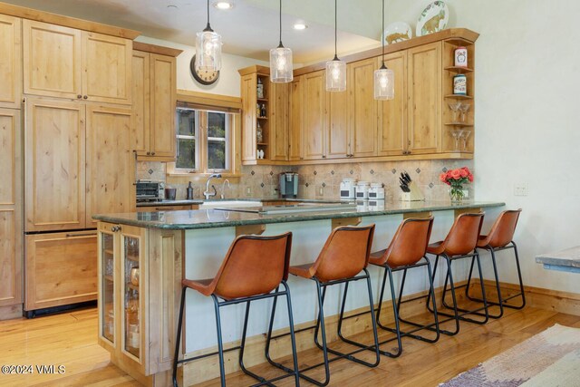 kitchen with light brown cabinetry, hanging light fixtures, kitchen peninsula, and dark stone countertops