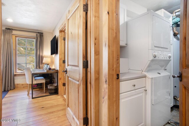 laundry room featuring cabinets, light hardwood / wood-style flooring, and stacked washer and clothes dryer