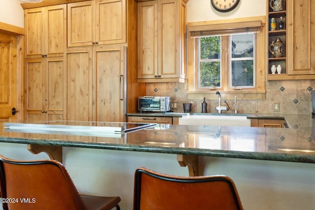 kitchen with tasteful backsplash, sink, a breakfast bar area, and dark stone countertops