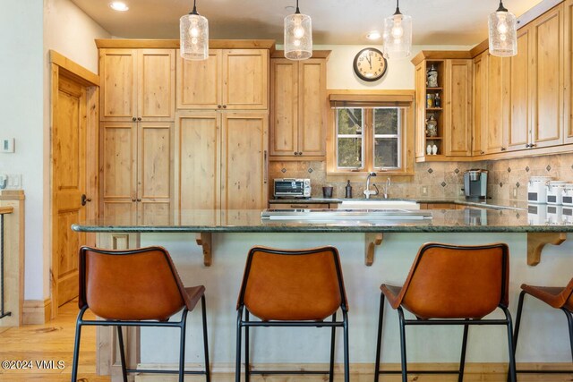 kitchen featuring pendant lighting, a breakfast bar area, dark stone countertops, backsplash, and light wood-type flooring