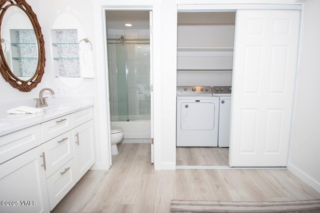 bathroom with toilet, combined bath / shower with glass door, vanity, separate washer and dryer, and wood finished floors