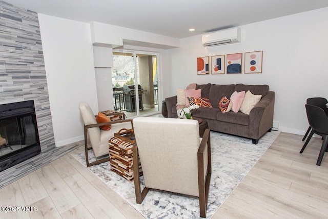 living room with a wall unit AC, light wood-style flooring, a fireplace, and baseboards