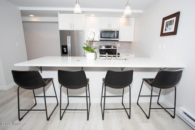 kitchen featuring stainless steel appliances, decorative backsplash, a baseboard heating unit, white cabinetry, and a kitchen breakfast bar