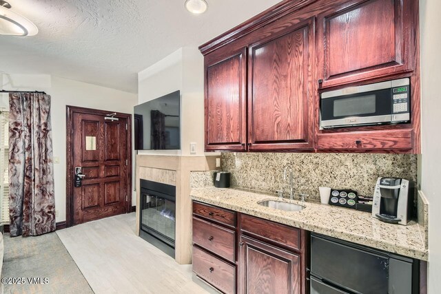 kitchen with sink, beverage cooler, backsplash, light stone counters, and a textured ceiling