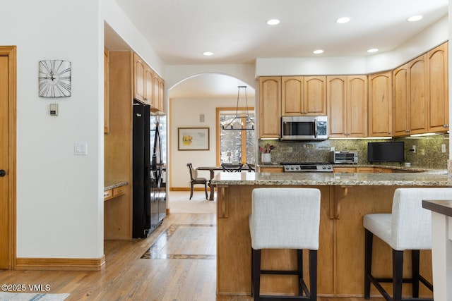2 Anvil Cir, Edwards, CO 81632 - kitchen featuring stainless steel microwave, black refrigerator, arched walkways, light wood-type flooring, and light stone counters