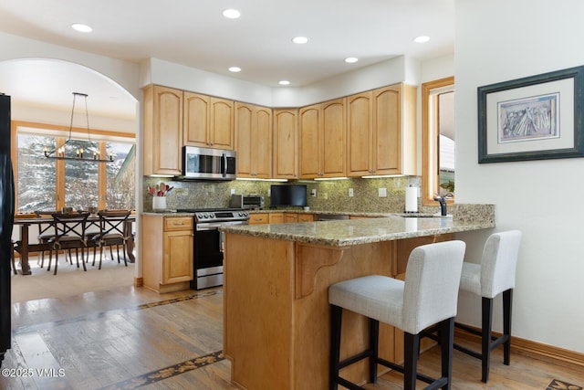 2 Anvil Cir, Edwards, CO 81632 - kitchen with appliances with stainless steel finishes, a breakfast bar, tasteful backsplash, light stone countertops, and light wood-style floors