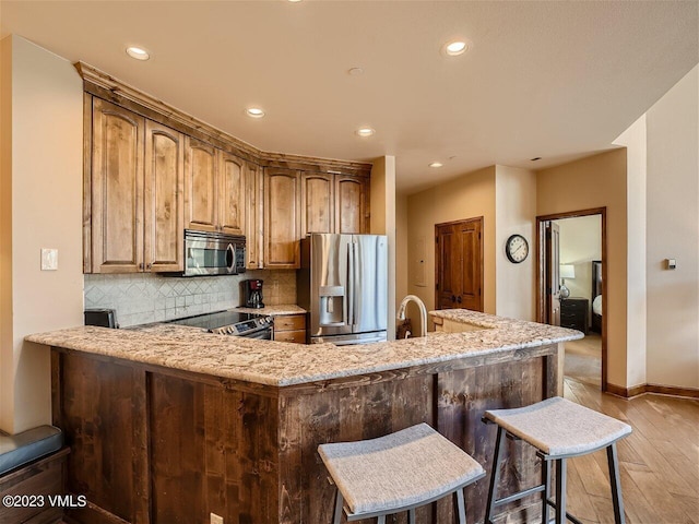 kitchen with light stone counters, recessed lighting, stainless steel appliances, light wood-type flooring, and backsplash