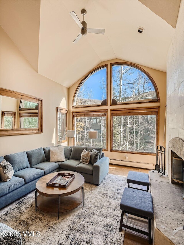 living room featuring high vaulted ceiling, a ceiling fan, a baseboard heating unit, wood finished floors, and a tile fireplace