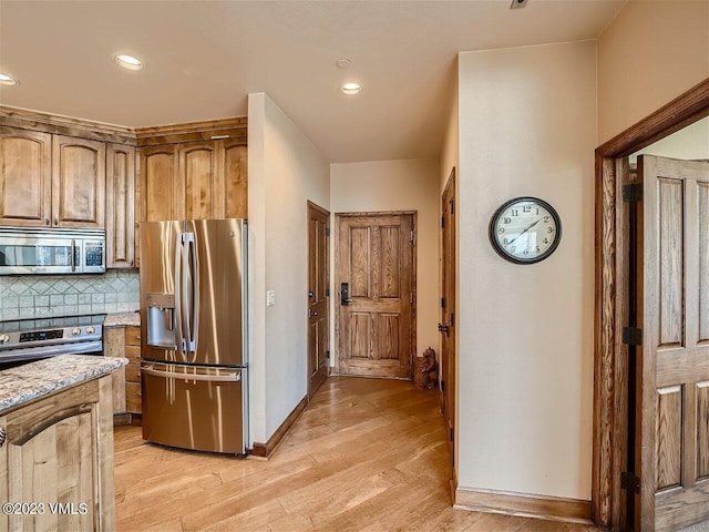 kitchen with tasteful backsplash, baseboards, light stone countertops, light wood-type flooring, and appliances with stainless steel finishes