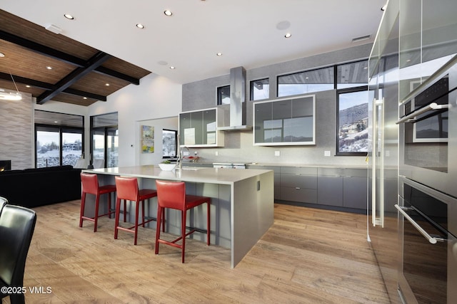 kitchen featuring a large island, light hardwood / wood-style flooring, gray cabinetry, beam ceiling, and a kitchen bar