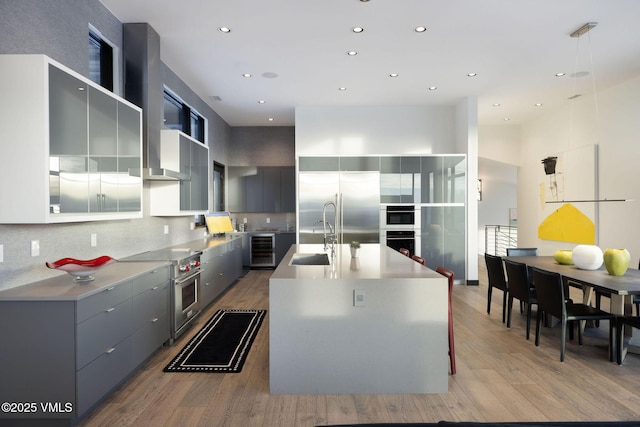 kitchen featuring sink, high quality appliances, wine cooler, an island with sink, and light wood-type flooring