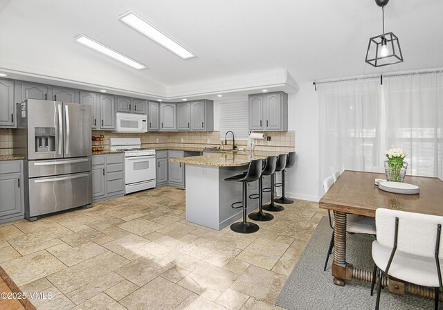 kitchen featuring sink, light stone counters, decorative light fixtures, gray cabinets, and white appliances