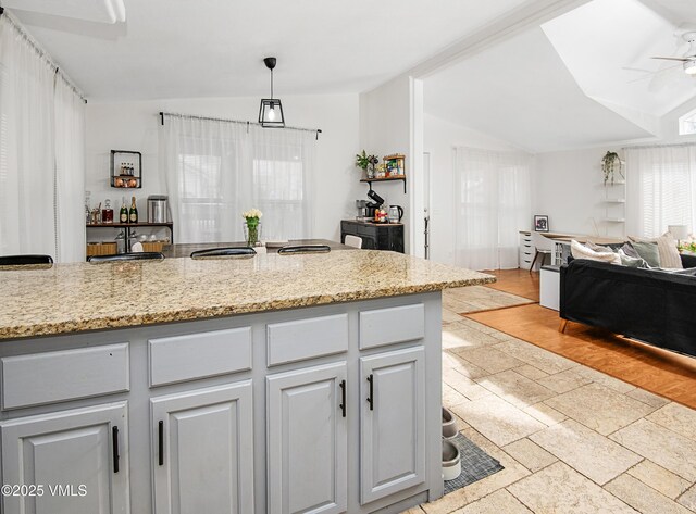 kitchen with gray cabinets, ceiling fan, light stone countertops, decorative light fixtures, and vaulted ceiling