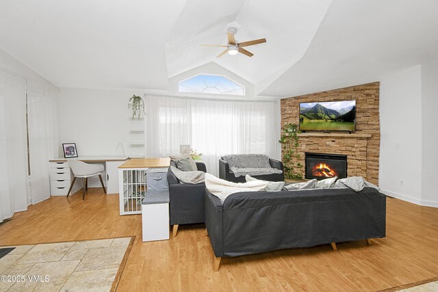 living room featuring lofted ceiling, a stone fireplace, light hardwood / wood-style flooring, and ceiling fan