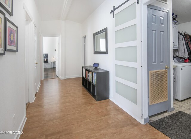 hall featuring washer / clothes dryer, a barn door, lofted ceiling with beams, and light hardwood / wood-style flooring