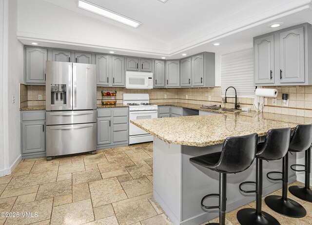 kitchen with lofted ceiling, sink, white appliances, gray cabinetry, and kitchen peninsula