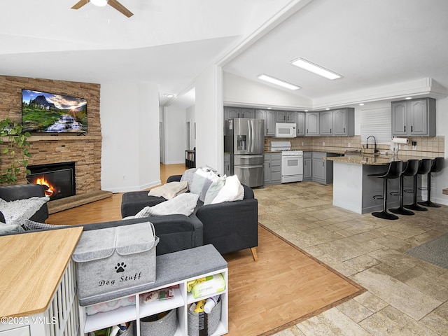 living room featuring a fireplace, vaulted ceiling, sink, and ceiling fan