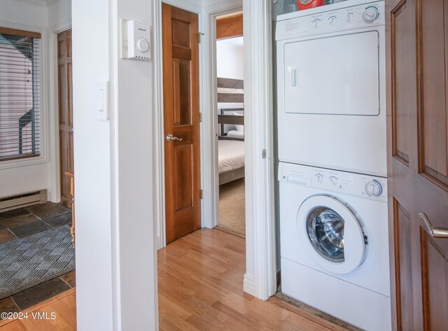 laundry area featuring light hardwood / wood-style floors, baseboard heating, and stacked washing maching and dryer