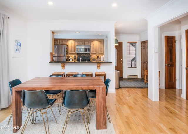 dining area featuring ornamental molding, a baseboard heating unit, and light hardwood / wood-style flooring