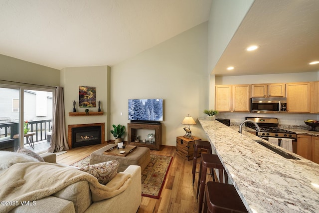 living area featuring recessed lighting, light wood-style flooring, a glass covered fireplace, and vaulted ceiling
