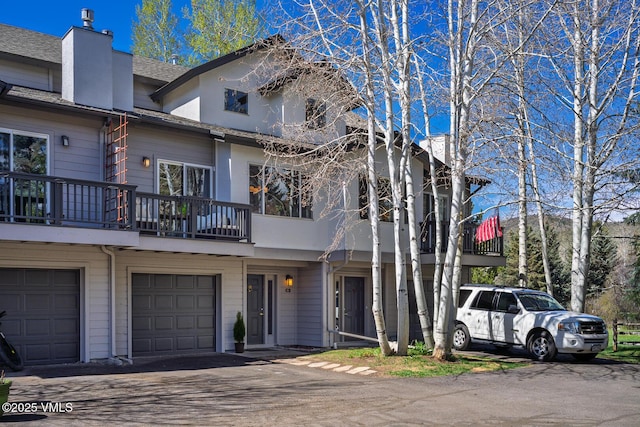 townhome / multi-family property featuring a garage, a chimney, roof with shingles, and a balcony