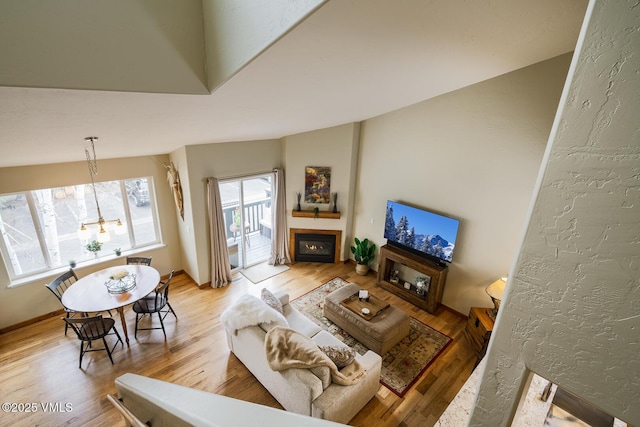 living area featuring an inviting chandelier, a lit fireplace, and wood finished floors