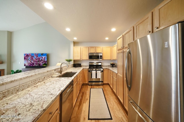 kitchen with light brown cabinetry, light wood-style floors, light stone counters, a sink, and appliances with stainless steel finishes