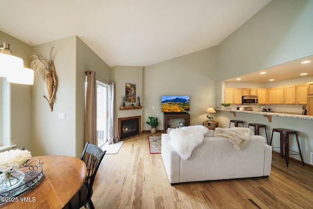 living area featuring a glass covered fireplace, recessed lighting, vaulted ceiling, and light wood finished floors
