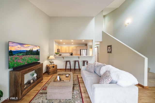 living room with stairs, a towering ceiling, baseboards, recessed lighting, and light wood finished floors