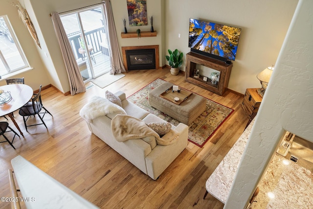 living area with baseboards, a glass covered fireplace, and wood finished floors