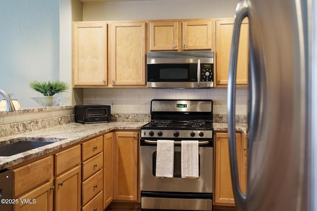 kitchen featuring light stone counters, a sink, appliances with stainless steel finishes, and backsplash