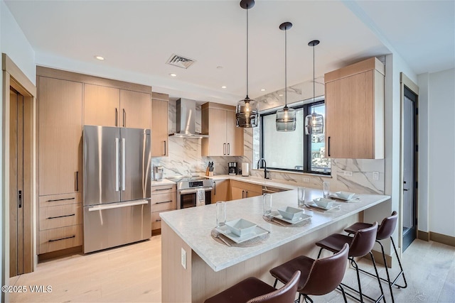 42 Riverfront Ln Unit 205, Avon, CO 81620 - kitchen with appliances with stainless steel finishes, wall chimney exhaust hood, a peninsula, and light wood-style floors