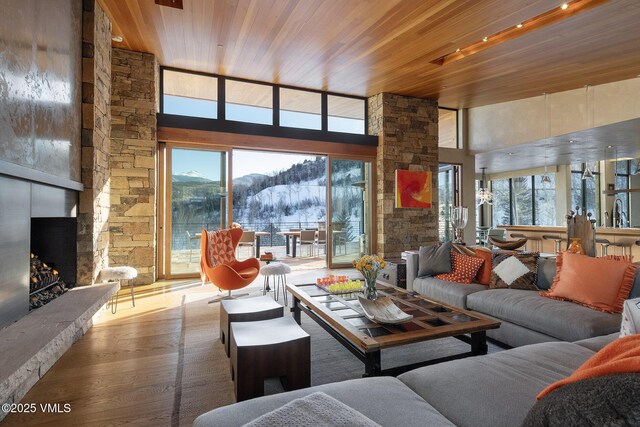 living room with a mountain view, a stone fireplace, a wealth of natural light, and wooden ceiling