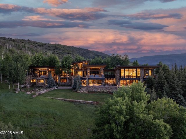 34 Whiskey Rdg, Edwards, CO 81632 - back of house at dusk featuring a mountain view, a yard, stone siding, and a balcony