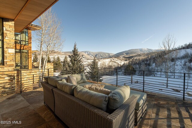 snow covered patio featuring a mountain view, an outdoor living space, and a balcony