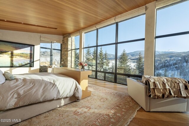 bedroom featuring a wall of windows, wood-type flooring, a mountain view, and wooden ceiling