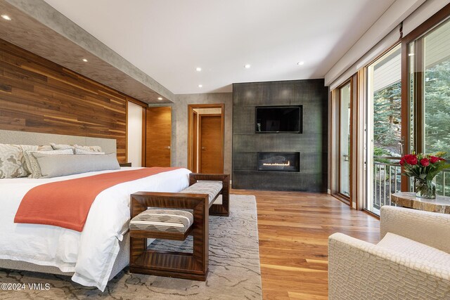 bedroom featuring recessed lighting, wood walls, wood finished floors, access to outside, and a tile fireplace