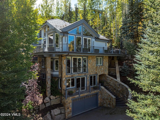 view of front facade with a balcony, stone siding, an attached garage, and stairs