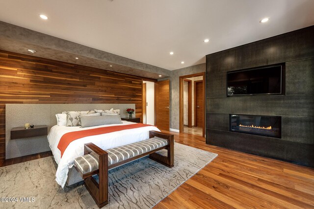 bedroom featuring recessed lighting, a large fireplace, wooden walls, and wood finished floors