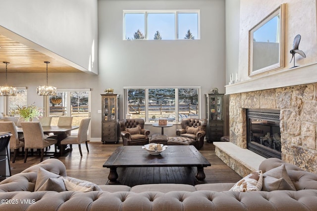 living area featuring a stone fireplace, wood finished floors, and a notable chandelier