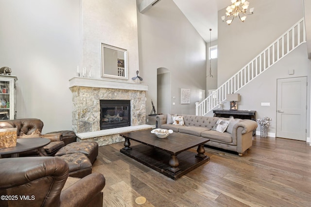 living area with a stone fireplace, wood finished floors, a towering ceiling, stairway, and an inviting chandelier