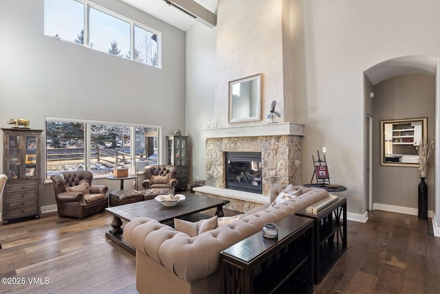 living room featuring a towering ceiling, baseboards, arched walkways, and wood finished floors