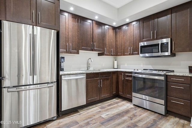 kitchen featuring appliances with stainless steel finishes, a sink, light wood-style flooring, and dark brown cabinets