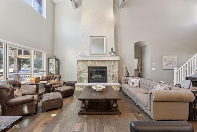 living room with arched walkways, a fireplace, stairway, a towering ceiling, and wood finished floors