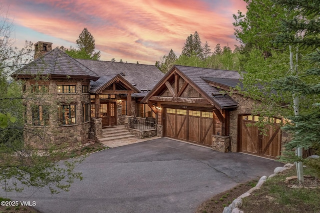 348 Red Draw, Edwards, CO 81632 - view of front of house featuring stone siding, a chimney, asphalt driveway, and an attached garage