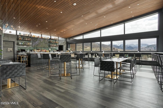 dining area with a wall of windows, hardwood / wood-style floors, bar area, a mountain view, and wooden ceiling