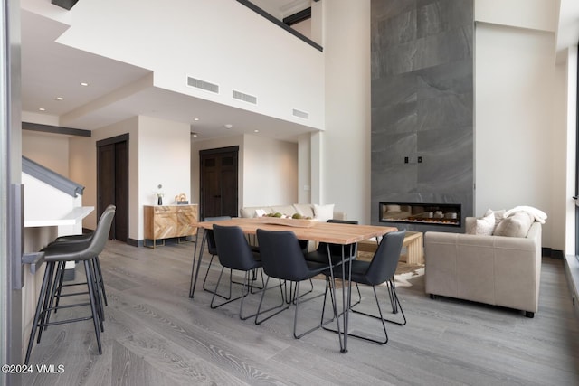 dining room featuring a tile fireplace, a towering ceiling, and light hardwood / wood-style flooring