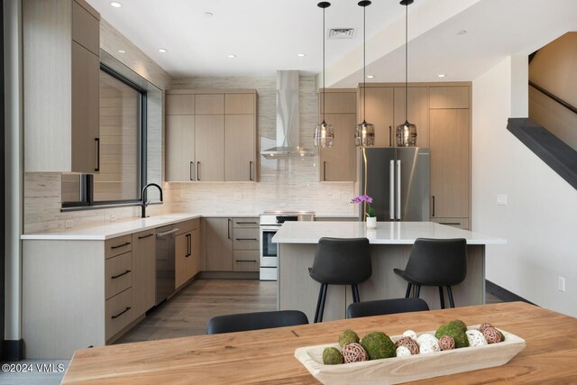 kitchen featuring a breakfast bar area, decorative light fixtures, a center island, stainless steel appliances, and wall chimney range hood